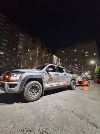 Грузовой автомобиль с прицепом, на котором находится легковой автомобиль, припаркован на дороге среди зелени