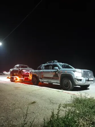 Грузовой автомобиль с прицепом, на котором находится легковой автомобиль, припаркован на дороге среди зелени