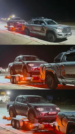 Грузовой автомобиль с прицепом, на котором находится легковой автомобиль, припаркован на дороге среди зелени