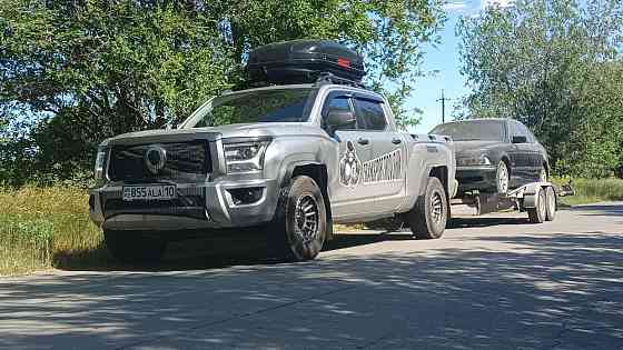 Грузовой автомобиль с прицепом, на котором находится легковой автомобиль, припаркован на дороге среди зелени