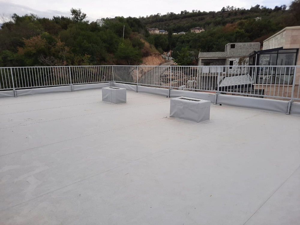 Жасыл төбелермен қоршалған, бетонды едені бар, қоршаумен қорғалатын шатырдағы алаңша, екі көтерілген элементімен.