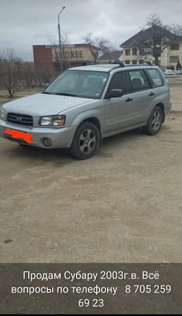 2003 жылғы Subaru сары түс, жол мен ғимараттардың фонында, төменде байланыс ақпараты.