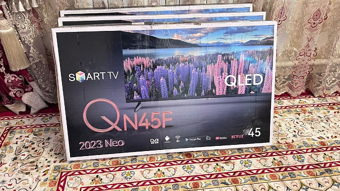 2023 жылғы Smart TV QN45F теледидарының қаптамасы, алдыңғы панелінде гүлденген өрістердің көрінісі