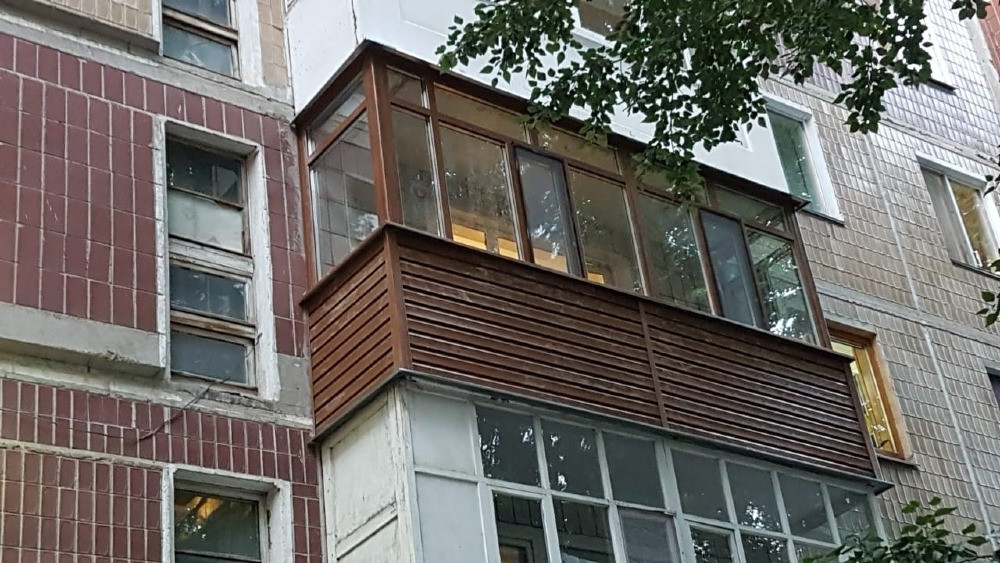 Ағаш бөліктері мен мөлдір кірістіктері бар балкон, көпқабатты үйдің фонында