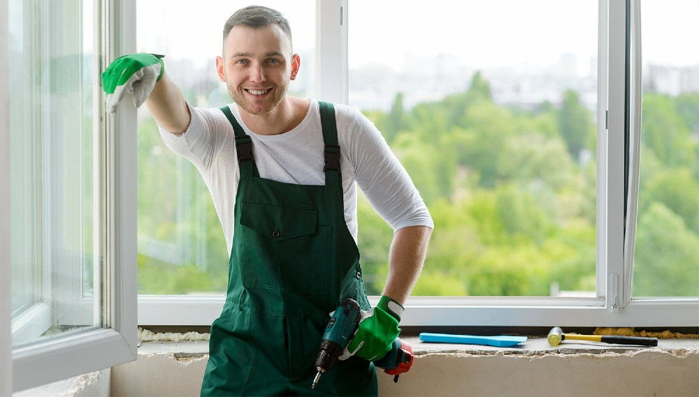 Рабочий в строительном комбинезоне пользователей чистит окно и улыбается на фоне зелени
