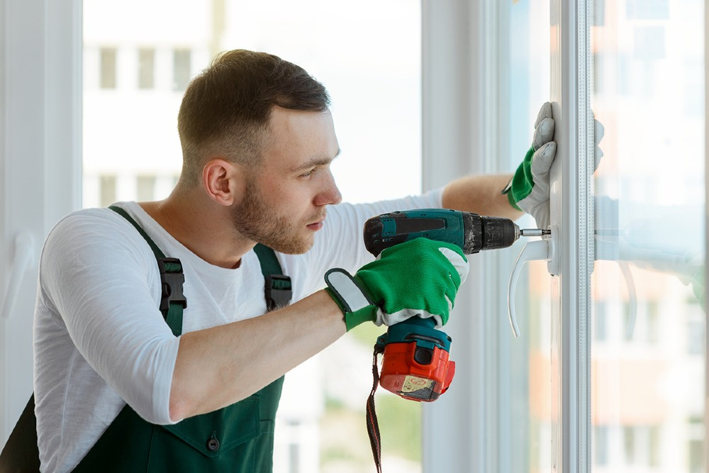 Мужчина с дрелью устанавливает стекло в окне, сосредоточенно работает с инструментом