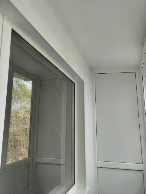 Угол остекленной лоджии с современными окнами и белыми стенами