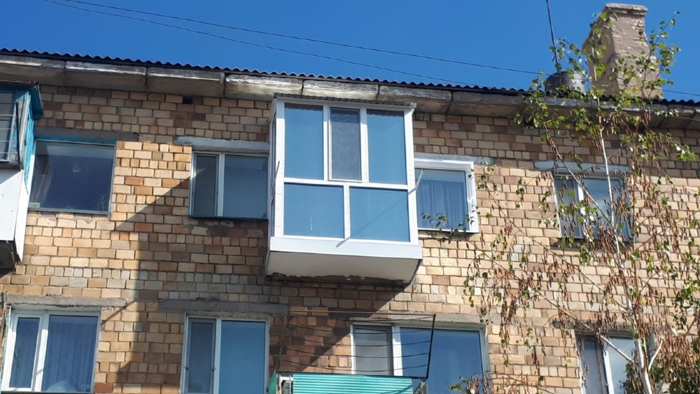 Балкон из стекла и металла на кирпичном доме, отражающий солнечный свет