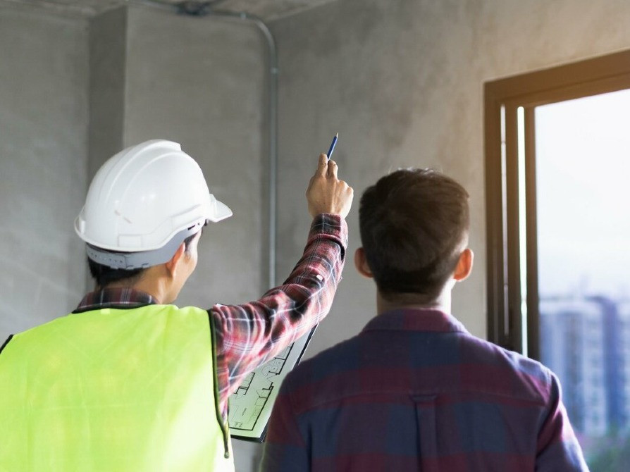 Бір топ жұмысшылар құрылыс алаңында жобаны талқылап жатыр, қолдарында жоспар бар