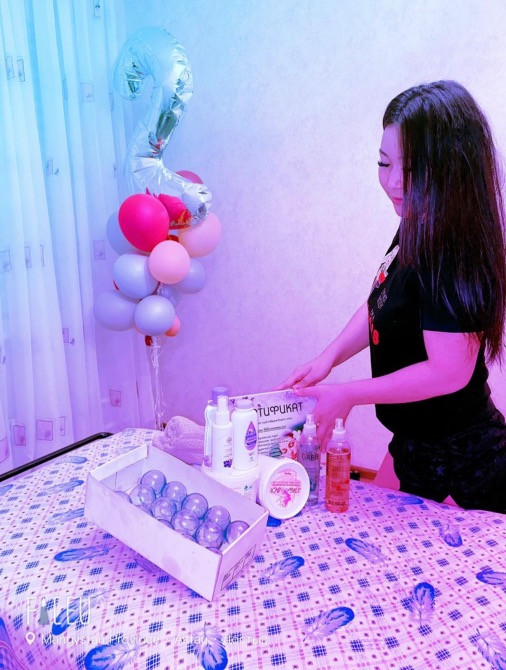 Қыз үстелдегі косметикалық өнімдерге, артқы пландағы шариктермен назар аударады.