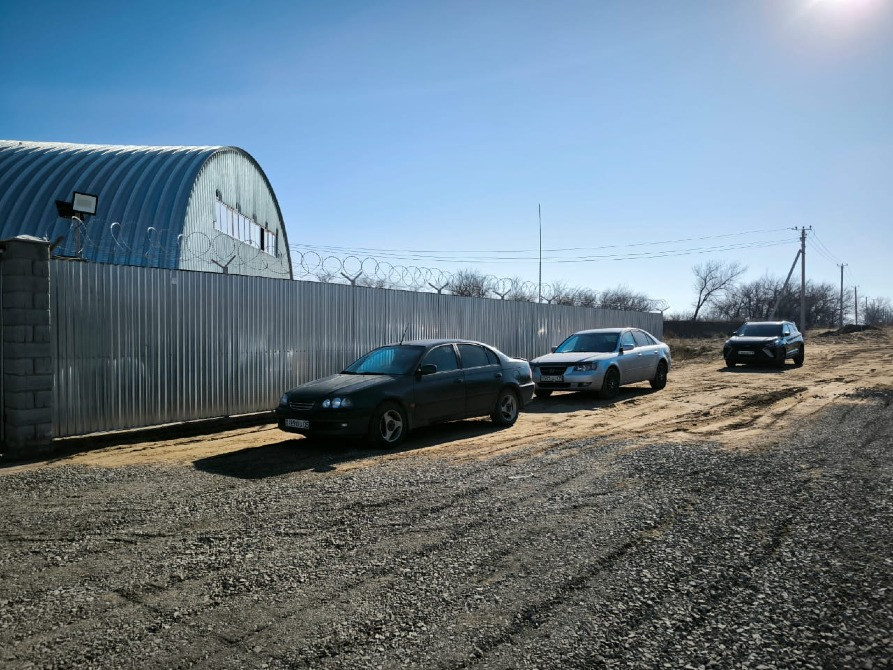 Ғимараттың жанындағы асфальтталмаған жолда тұрған автомобильдер