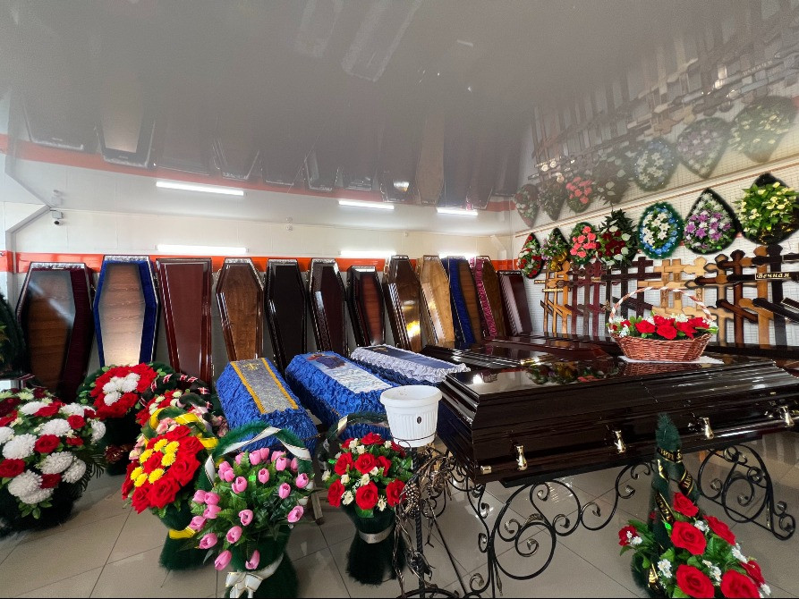 Внутренний вид ритуального магазина с различными гробами и цветами для оформления похорон
