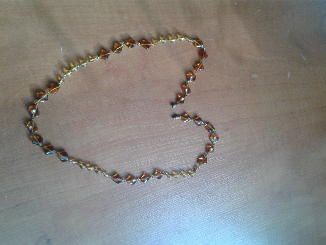 Алтын түсті моншақтардан жасалған және ағаш бетінде орналасқан жүрек пішінді зергерлік бұйымның суреті.