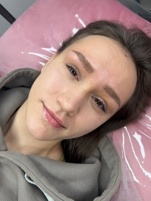 Сұр худиде киінген қыз, кушеткеде жатып, жеңіл макияжбен, күлімсіреп отыр