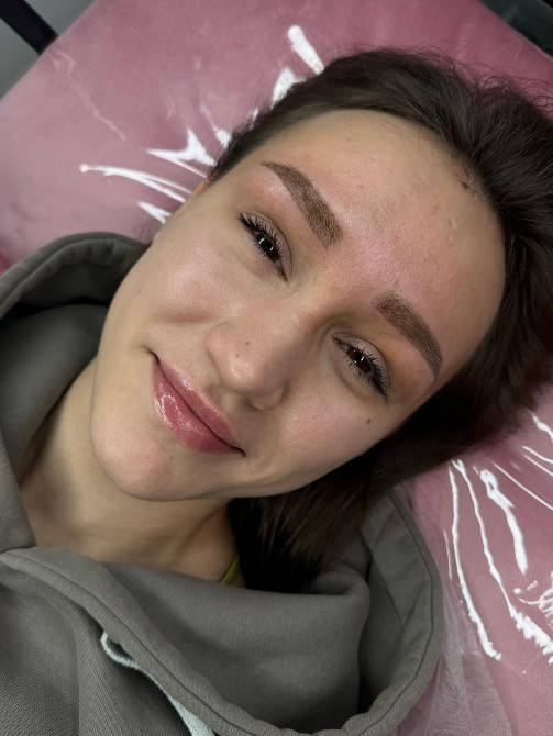 Сұр худиде киінген қыз, кушеткеде, жеңіл макияжбен процессқа рахаттанып отыр