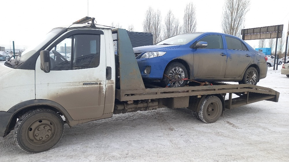 Грузовик с синей машиной на эвакуаторе в зимних условиях