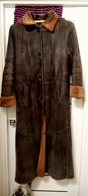 Долгое коричневое пальто из замши с воротником и манжетами из меха, висящее на дверце