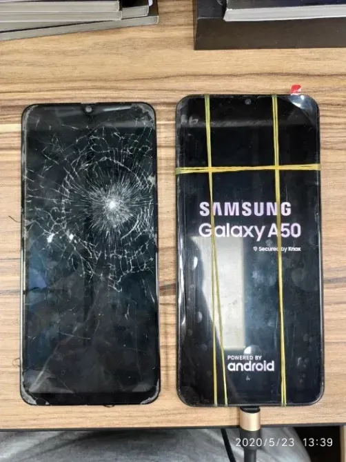 Екі смартфон, біреуі жарықшақтанған экранмен, екіншісі жанып тұрған, Samsung Galaxy A50 логотибін көрсетіп тұр