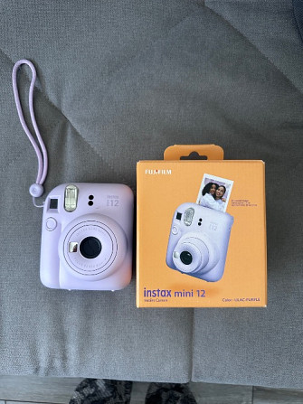 Камера Instax Mini 12 в светлом цвете с упаковкой, лежащая на сером фоне