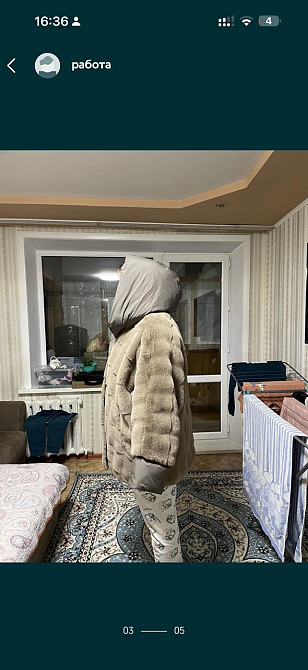 Мужчина в теплой одежде стоит спиной к камере в комнате с окном