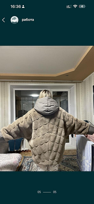 Мужчина в теплой одежде с капюшоном и поднятыми руками в комнате с окном