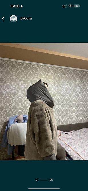 Мужчина в теплой одежде стоит в комнате с обоями и мебелью