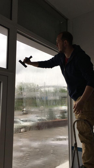 Ер адам ғимаратта әйнекті тазартады