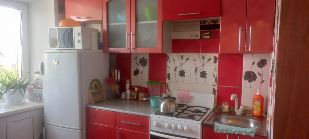 Ас бөлмесі қызыл шкафтармен, плита мен тоңазытқышпен