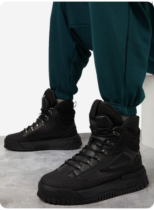 Черные кроссовки на ногах человека в зеленых спортивных штанах