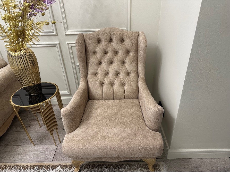 Кремді барқыт кресло, түймелерімен, дөңгелек үстелдің қасына орналастырылған