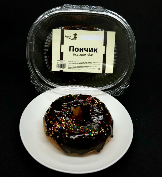 Шоколадты глазурьмен және себілген ұнтақпен пончик, ақ табақта.