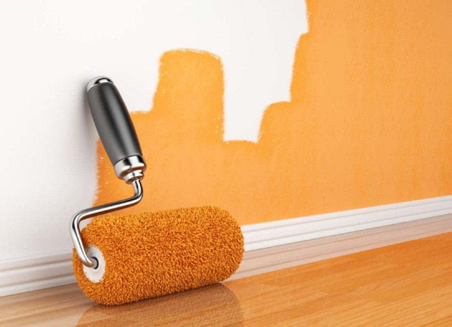 Валик для краски с черной ручкой, окрашивающий стену в оранжевый цвет, рядом с деревянным полом