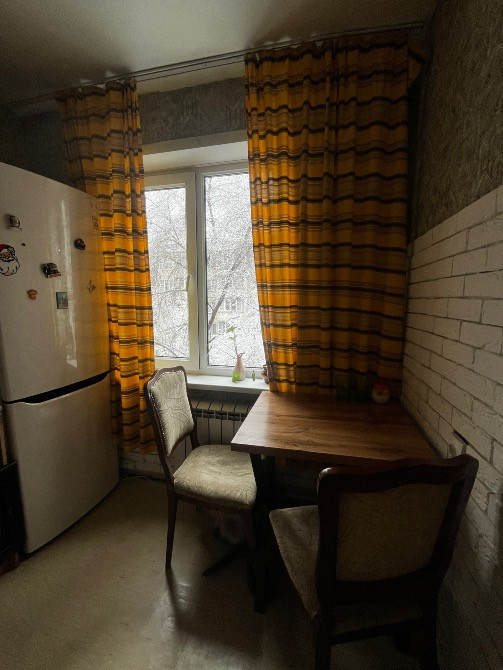 Терезе жанындағы дастархан мен орындықтармен жайлы ас үй бұрышы, жарқын перделермен безендірілген