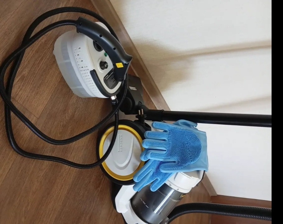 Паровой очиститель с шлангом, контейнером для воды и синими резиновыми перчатками на деревянном полу