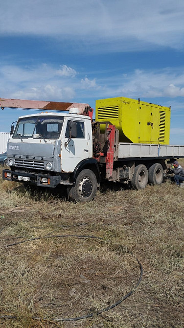 грузовой автомобиль белого цвета с желтым генератором на платформе и полем на заднем плане