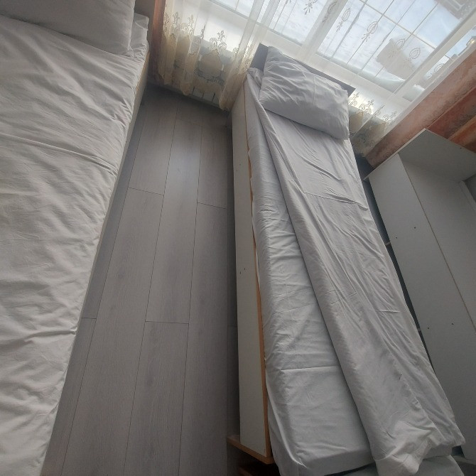 Төсек жабдықтары бар төсекке қарау, перделер арқылы күн сәулесі.