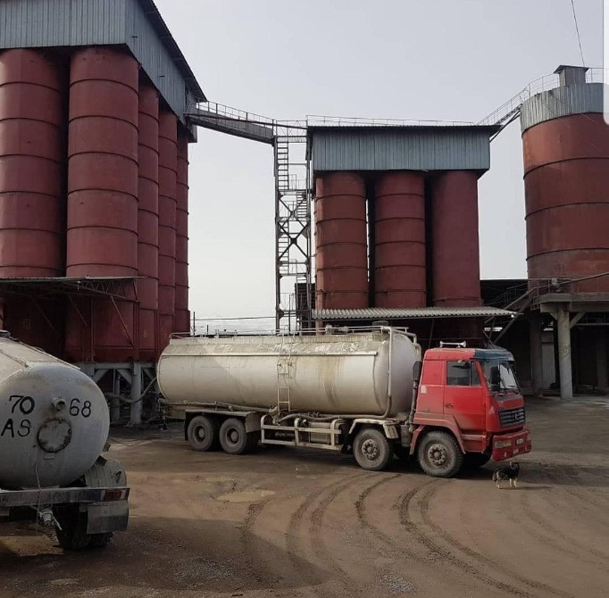 Завод с красными силосами и грузовиком, перевозящее материалы