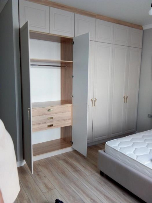 Открытый шкаф с ящиками и весами в светлом цвете рядом с кроватью