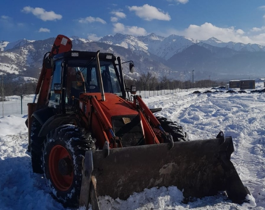 Бульдозер на фоне снежных гор и голубого неба. Снег вокруг машины, видно зимние условия работы техники