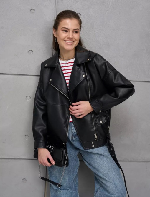 Женщина в черной кожаной куртке на фоне серой стены