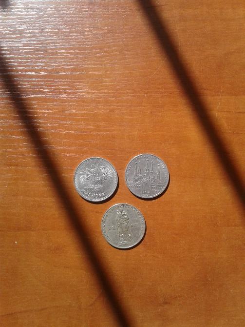 Три монеты на деревянной поверхности, светлые тени от предметов рядом