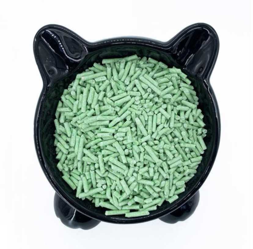 Чаша черного кота, наполненная зелеными гранулами для кошачьего туалета