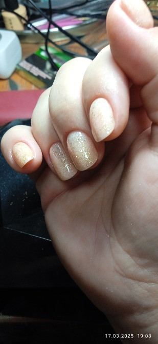 На фотографии изображены руки с маникюром, ногти искусственные с блестками, на фоне мебели