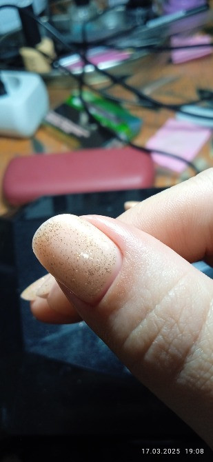 На фотографии отображены нюансы маникюра, близкий план того, как выглядит ноготь с блестками, на фоне рабочего стола