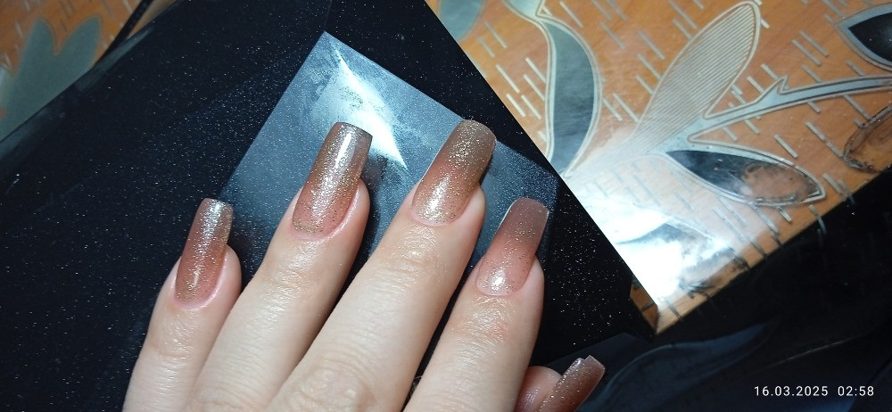 На фотографии представлены длинные ногти с градиентом и блестками, на фоне домашних предметов