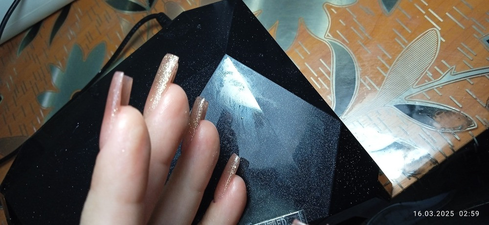 Показаны длинные ногти с блестящим покрытием, аккуратно оформленные, на фоне стола