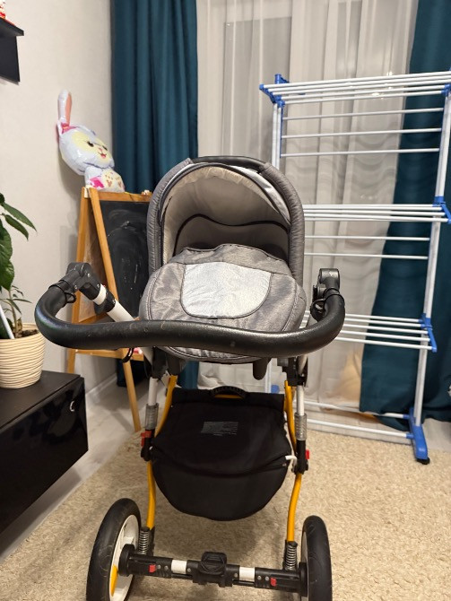 Коляска с серым козырьком, сфотографирована спереди в помещении