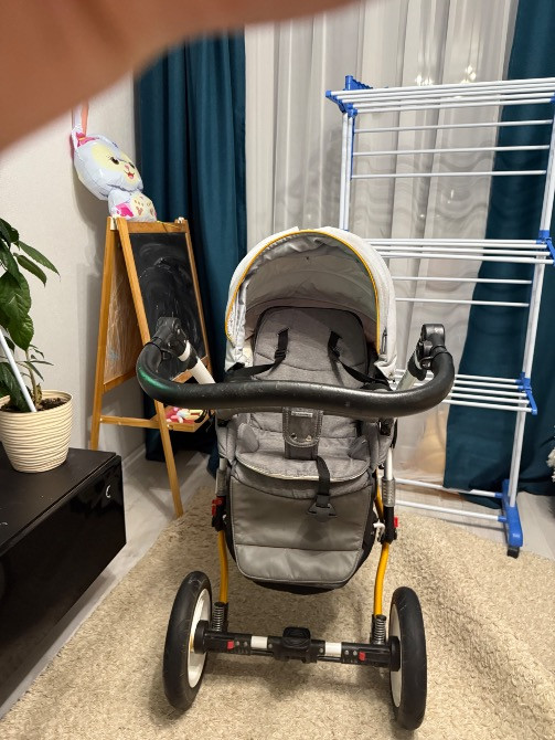 Коляска с серой обивкой, сфотографирована спереди в комнате