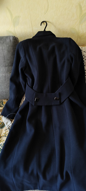 Задняя сторона темно-синего пальто на вешалке с поясом