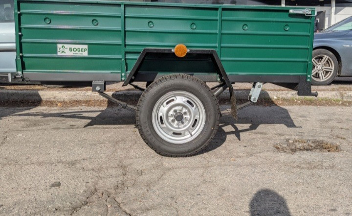 Боковой вид зеленого прицепа на фоне припаркованных автомобилей